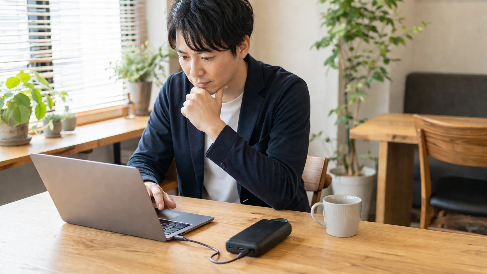 カフェでノートPCを使いながら、モバイルバッテリーの出力を確認しているビジネスパーソンの様子。